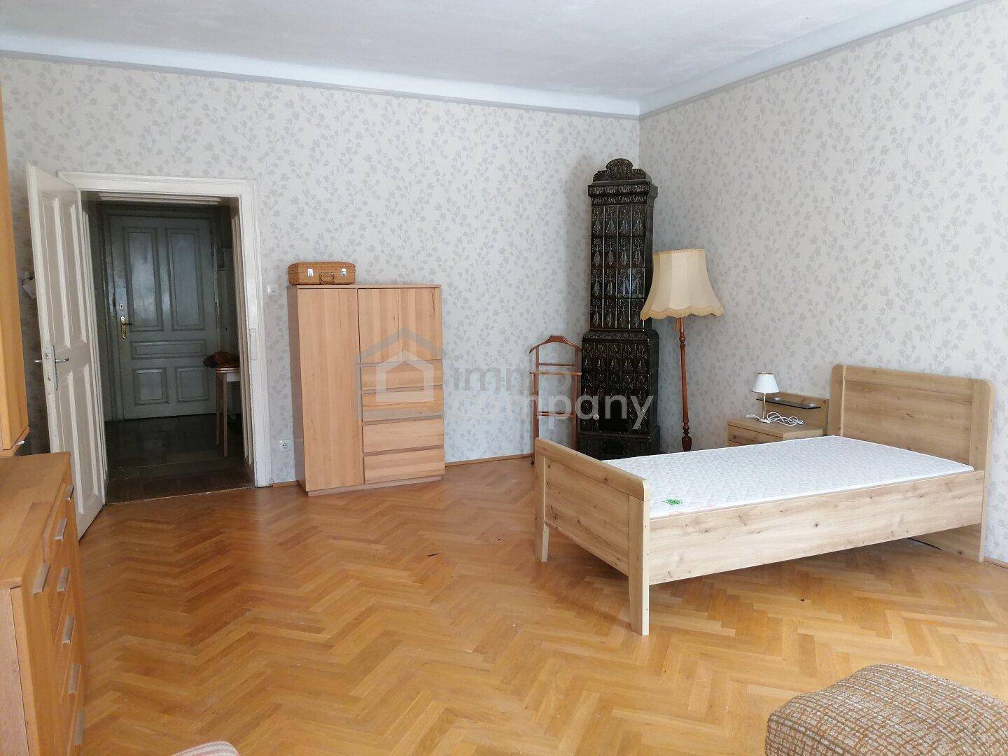 Helles Schlafzimmer mit Einzelbett, Kleiderschrank und einem dekorativen Kachelofen.