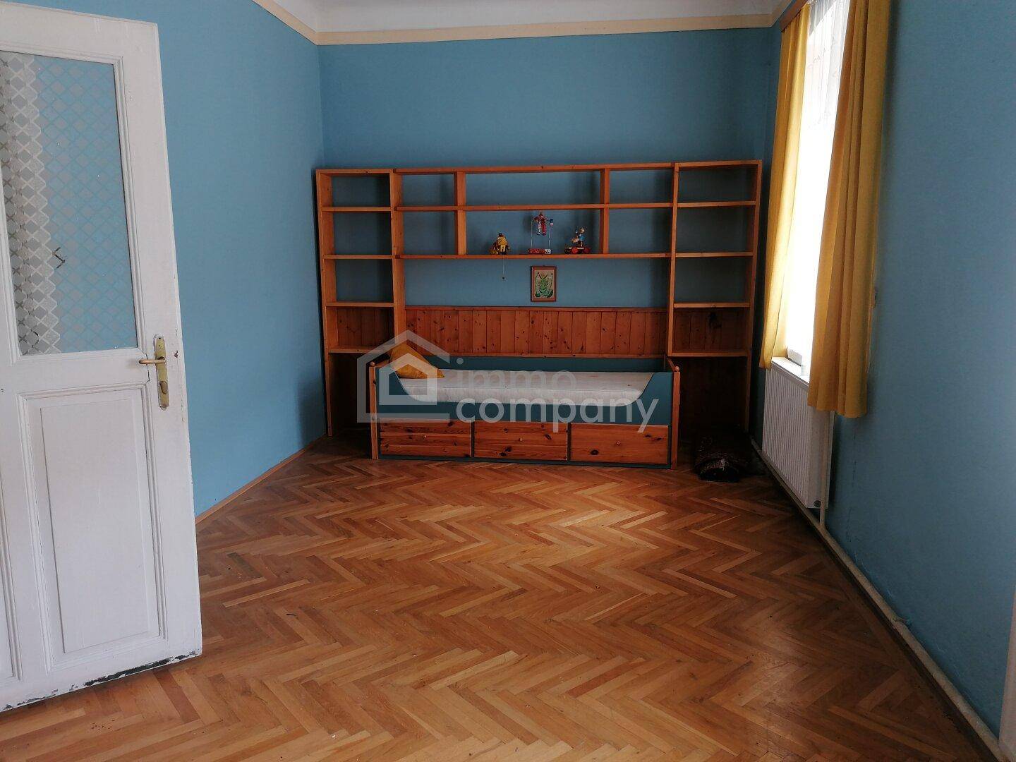 Kinderzimmer oder Gästezimmer mit blauen Wänden und integriertem Holzregalsystem.