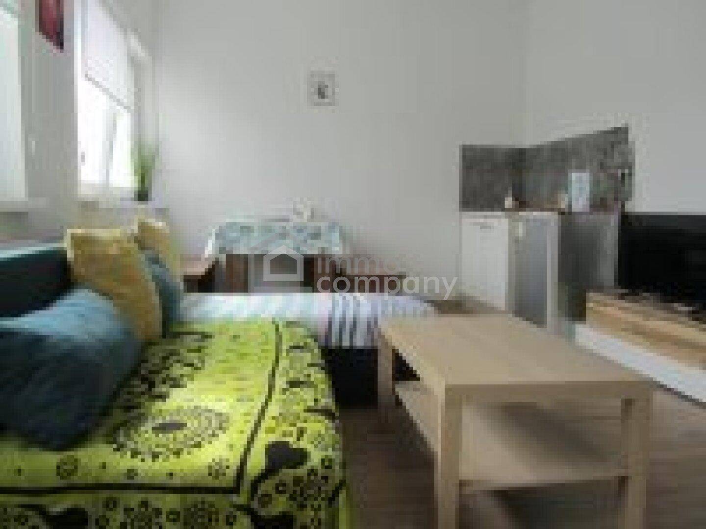 Gemütlicher Wohnbereich mit Sofa, Couchtisch, kleinem Essbereich und integrierter Küchenzeile.