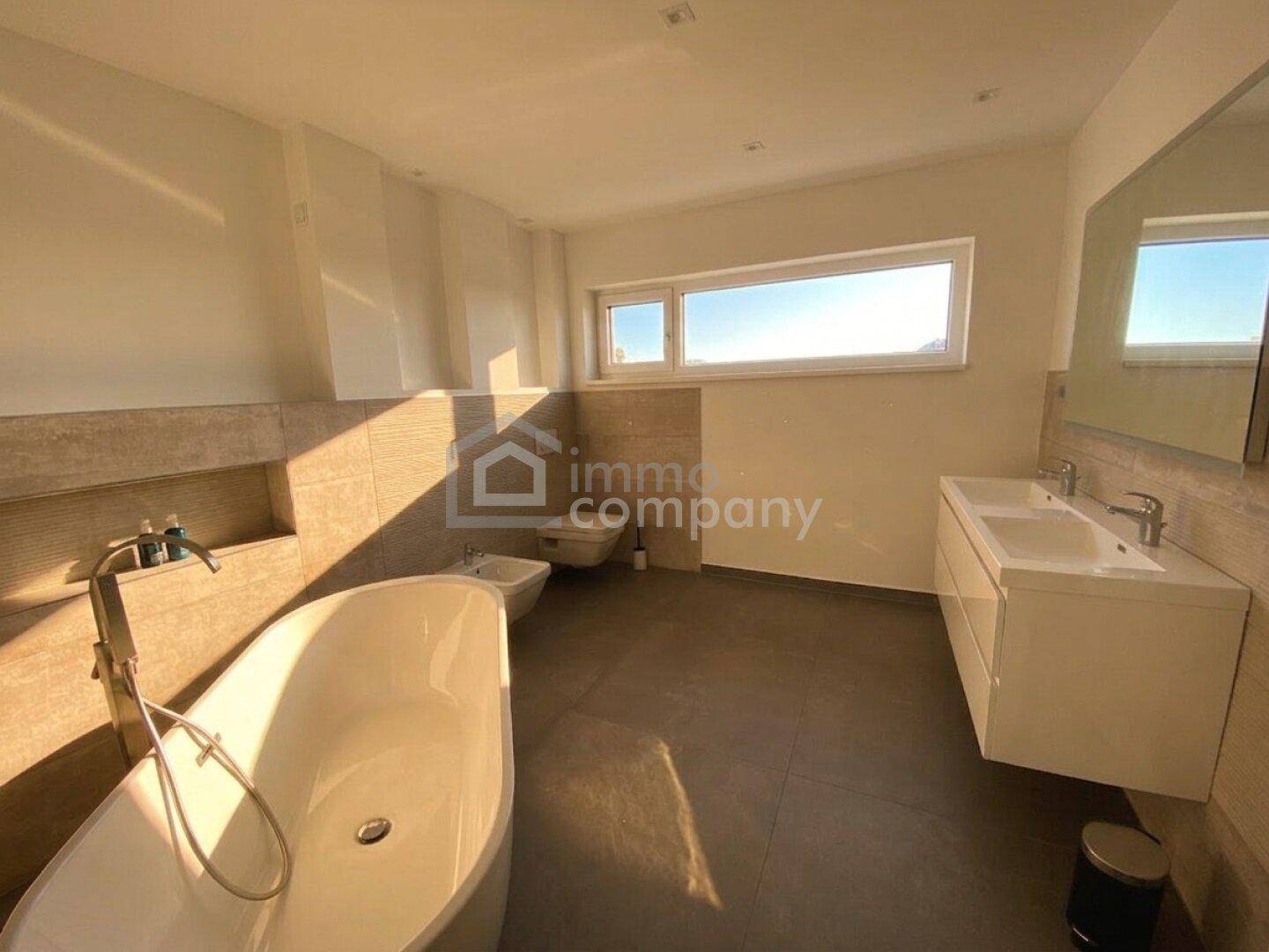 Geräumiges Badezimmer mit freistehender Badewanne, Doppelwaschbecken und Fenster.