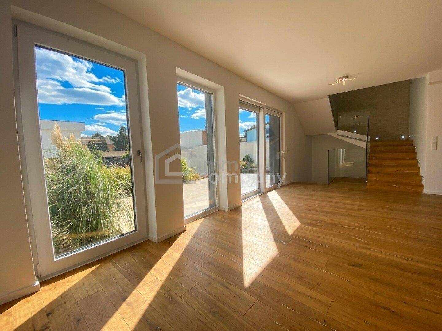 Lichtdurchfluteter Wohnbereich mit Holzboden, großen Fenstern und Blick ins Grüne.