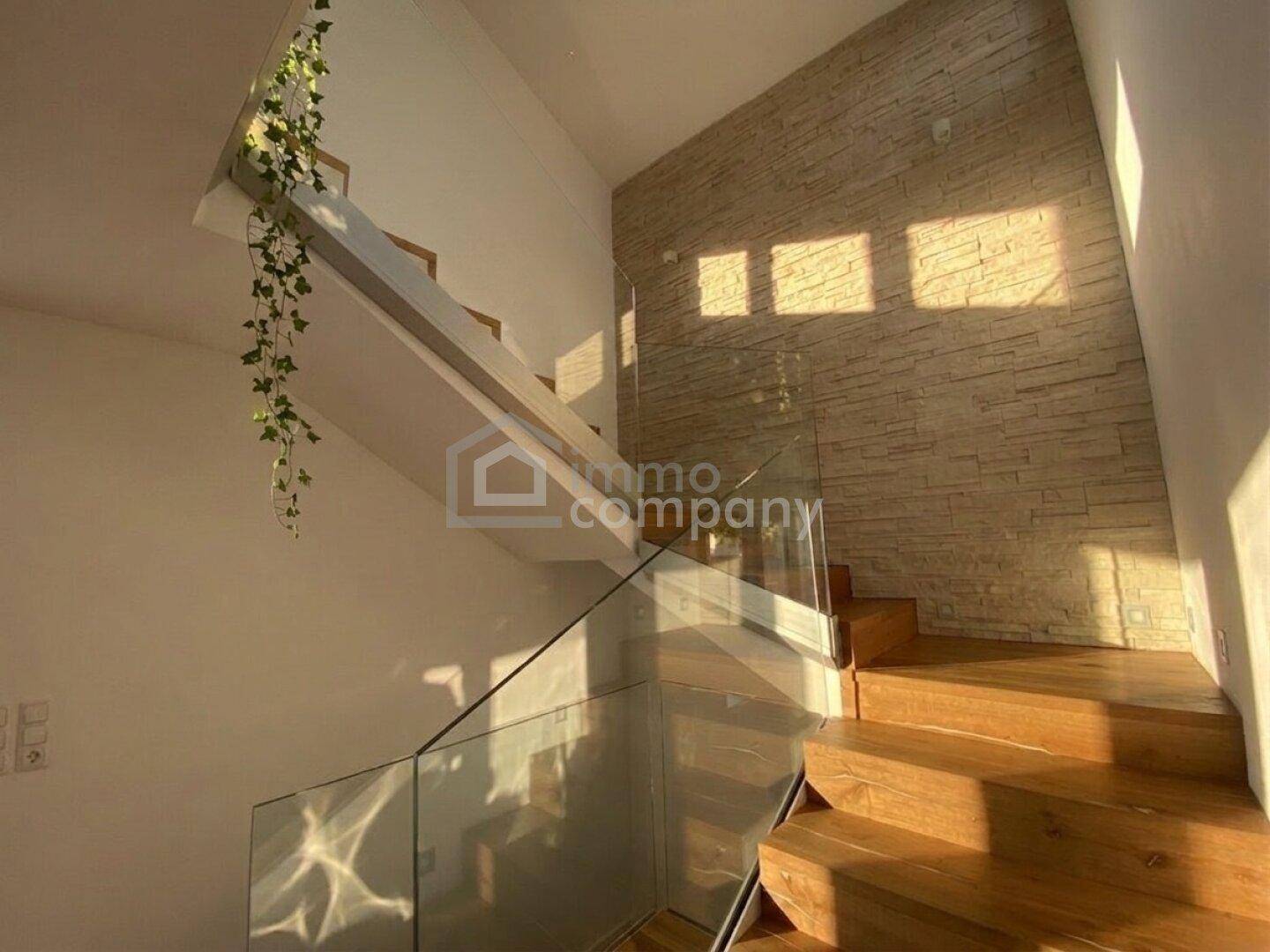 Moderner Treppenaufgang mit Holzstufen, Glasgeländer und dekorativer Steinwand.
