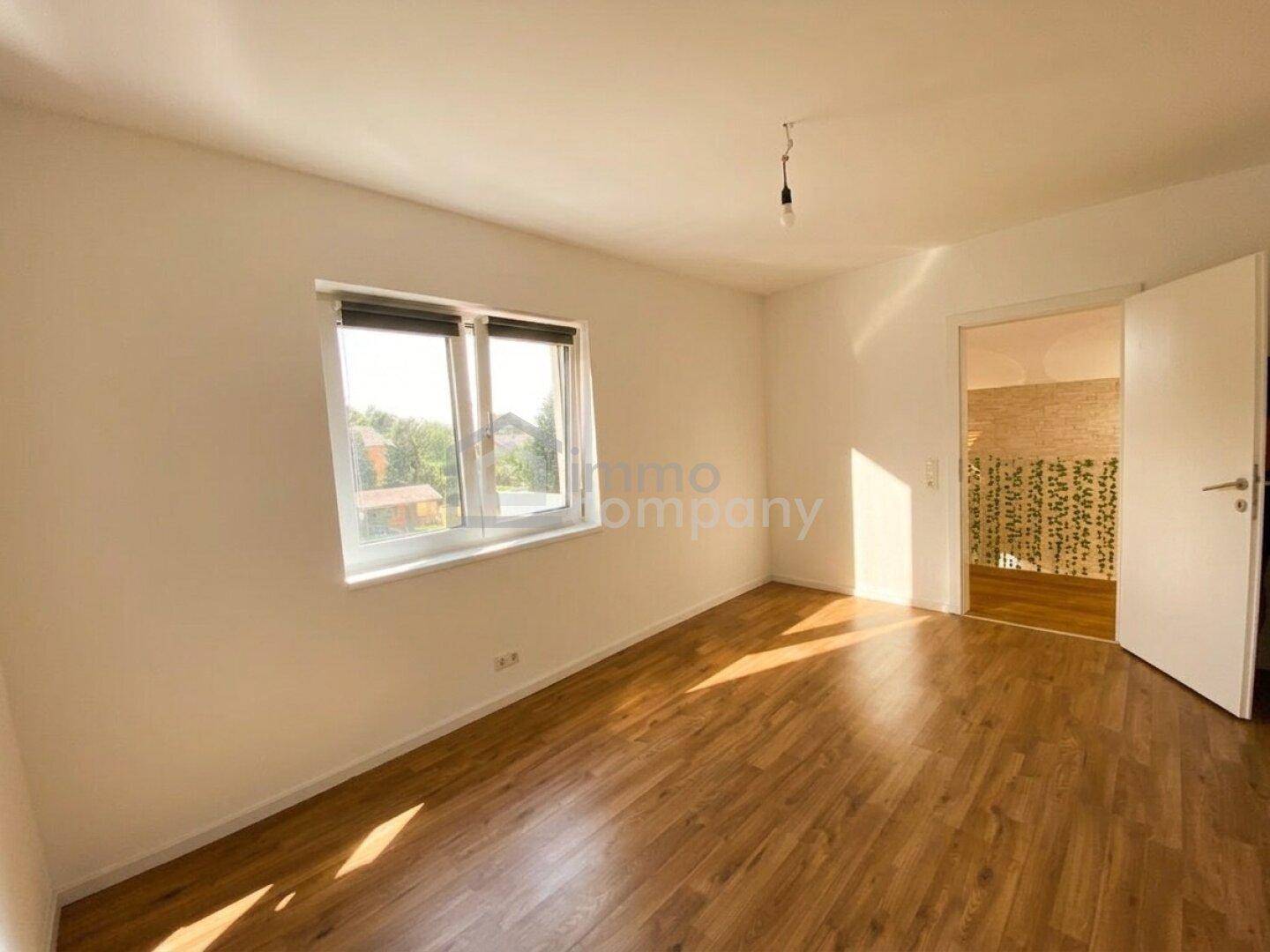 Geräumiges Schlafzimmer mit Holzboden und Fenster, das viel Tageslicht hereinlässt.
