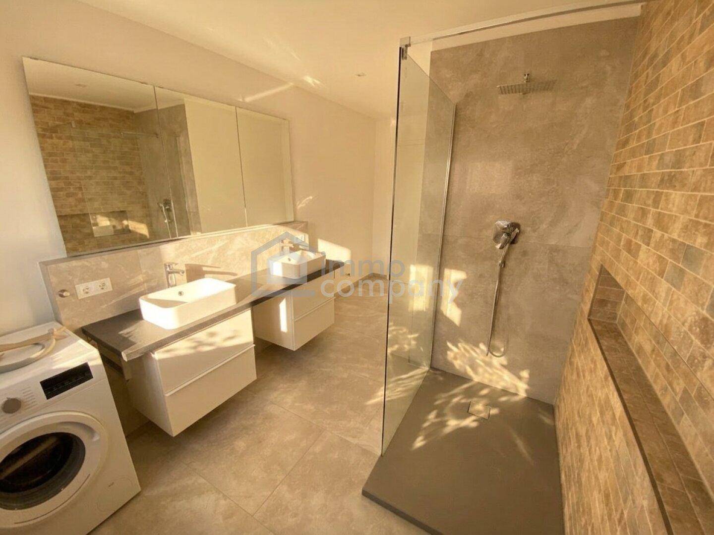 Modernes Badezimmer mit begehbarer Dusche, Doppelwaschbecken und Waschmaschine.