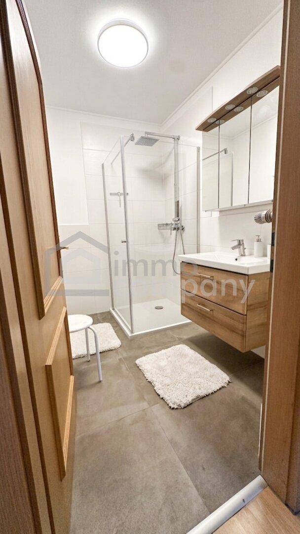 Modernes Badezimmer mit Glasdusche, Holzwaschtisch und Spiegelschrank, hell gefliest und funktional.