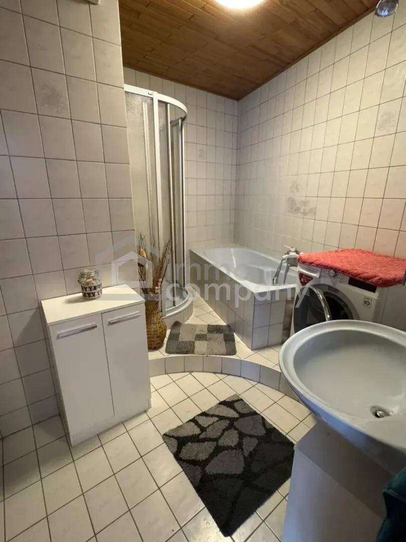 Badezimmer im Stil der 80er Jahre mit Duschkabine, Badewanne und Holzdecke.