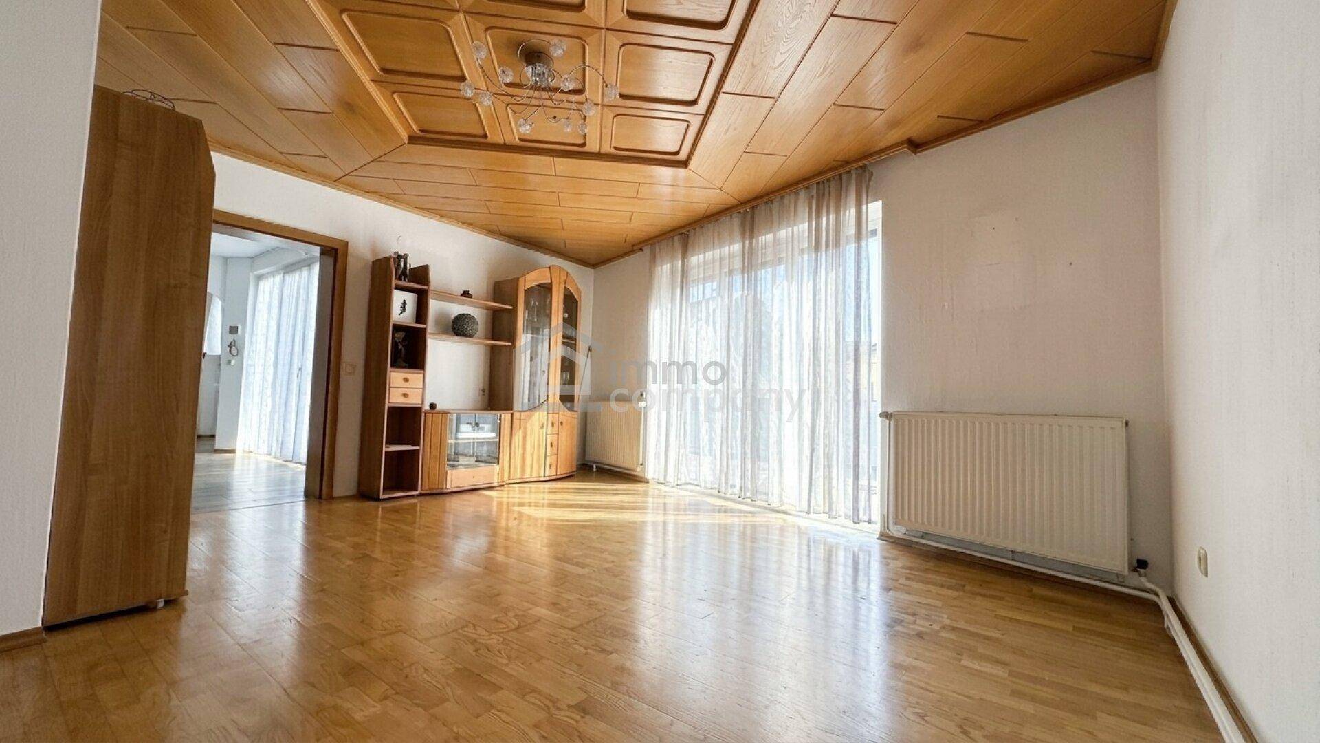 Helles Wohnzimmer mit dekorativer Holzdecke, Holzboden und großem Fenster, gut beleuchtet.