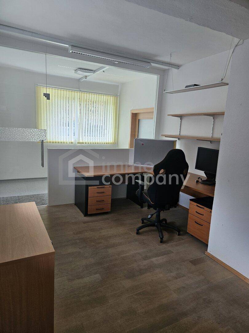 Modern eingerichtetes Büro mit Laminatboden, einem Schreibtisch und einem Fenster mit Jalousien.