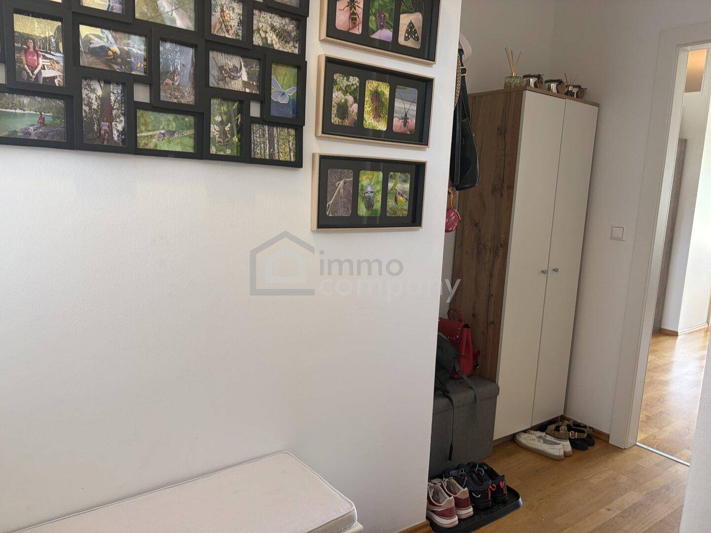 Heller Eingangsbereich mit Holzboden, Garderobenschrank und dekorativen Bilderrahmen an der Wand.