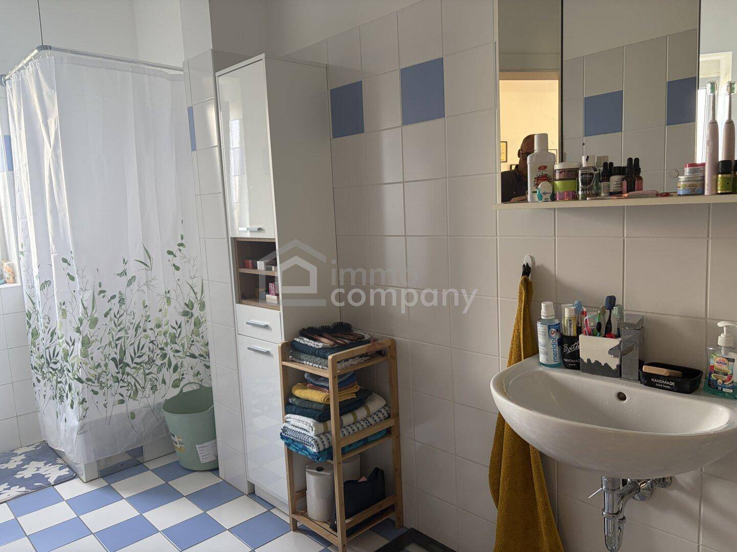 Badezimmer mit blauen und weißen Fliesen, Waschbecken und Duschbereich mit Vorhang.