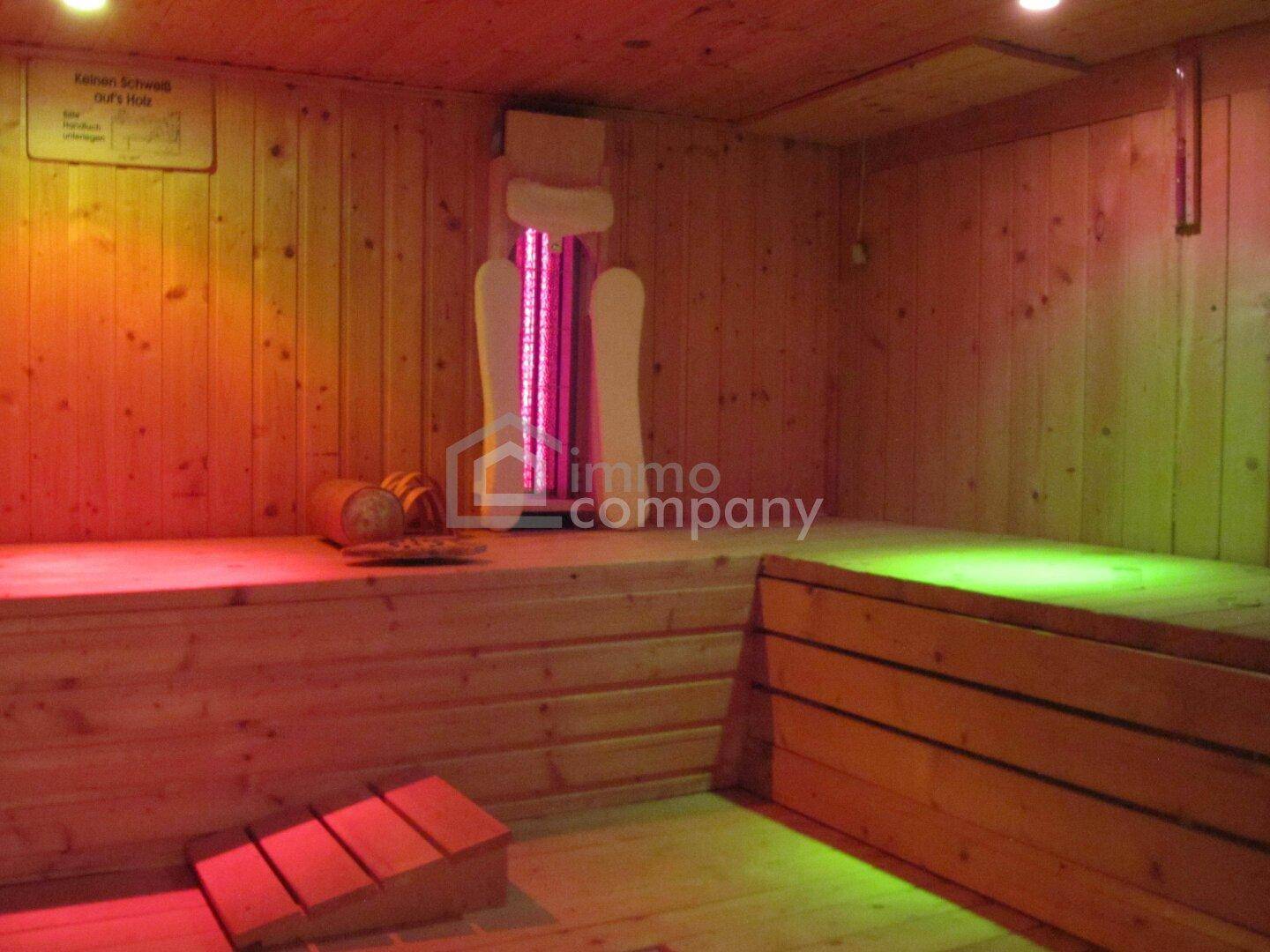 Gemütliche Holzsauna mit farbiger Beleuchtung und bequemen Bänken für private Wellnessmomente.