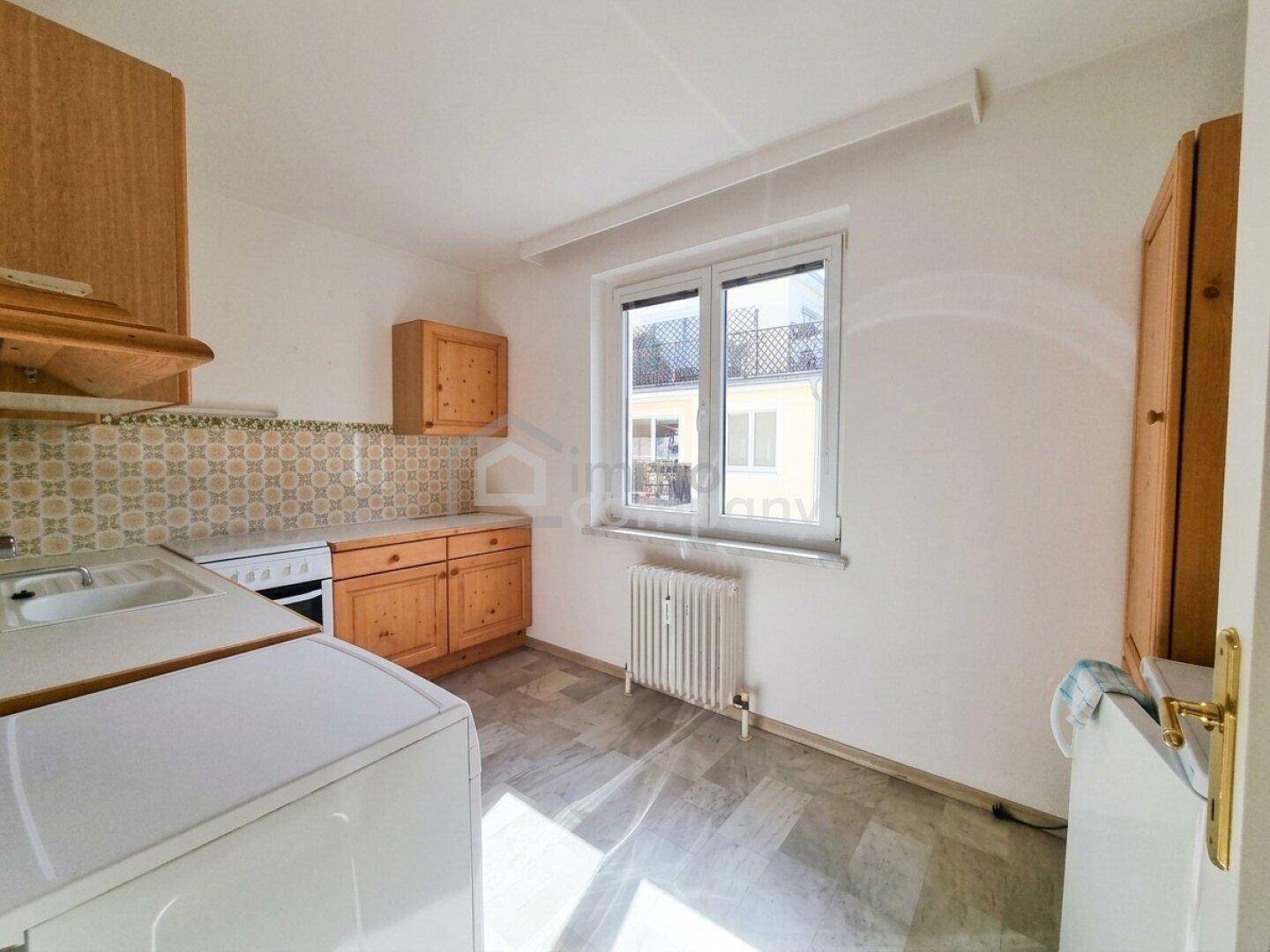 Funktionale Küche mit Holzschränken, weißen Geräten und einem Fenster mit Blick nach draußen.
