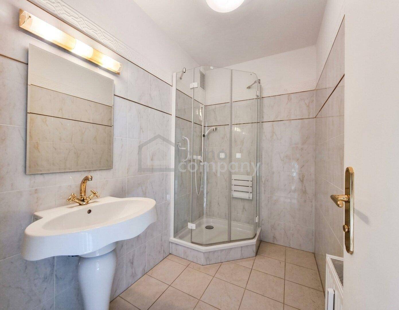 Gefliestes Badezimmer mit Eckdusche, Waschtisch und goldfarbenen Armaturen.
