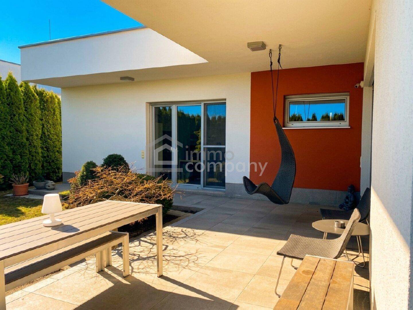 Überdachte Terrasse mit modernen Gartenmöbeln, Hängesessel und Zugang zum Gartenbereich.