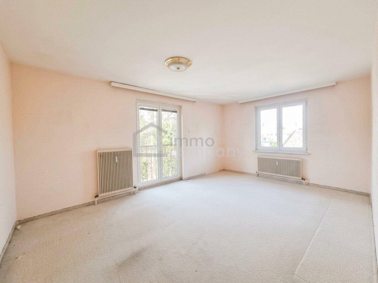 Geräumiges Schlafzimmer mit hellem Teppichboden, zwei Fenstern und Heizkörpern.