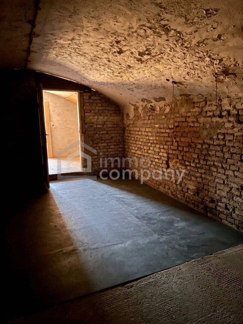 Historischer Kellerraum mit Ziegelwänden, Gewölbedecke und neuem Betonboden, hell durch den Eingang.
