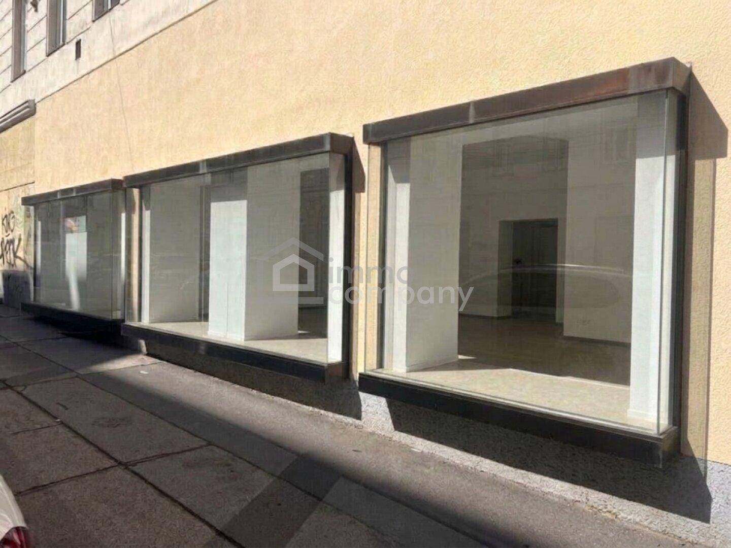 Drei große Schaufenster im Erdgeschoss eines Gebäudes, die leere Geschäftsräume mit Holzboden zeigen.