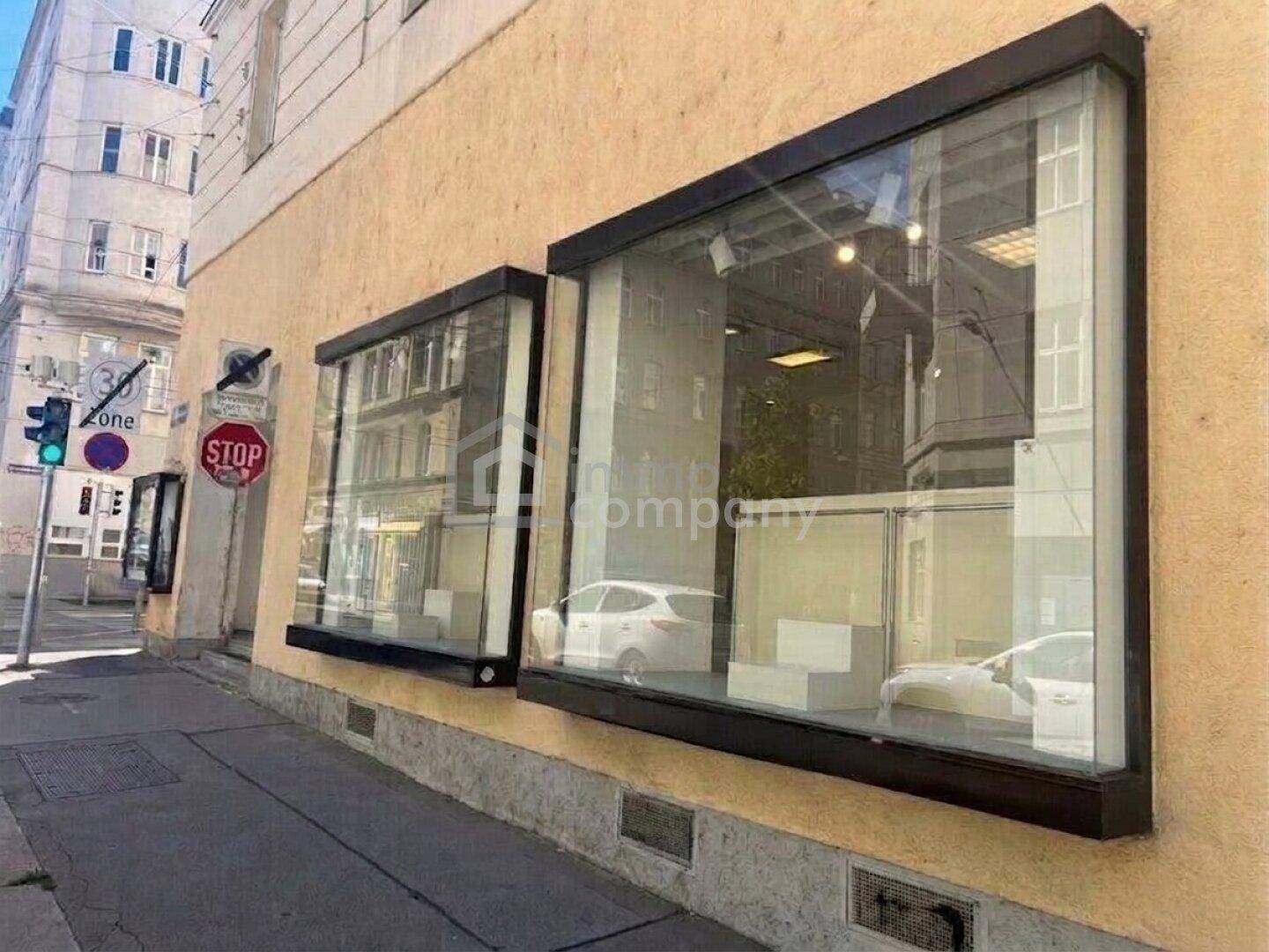 Zwei große Schaufenster eines Geschäftsraums im Erdgeschoss, die den Blick auf die Straße freigeben.