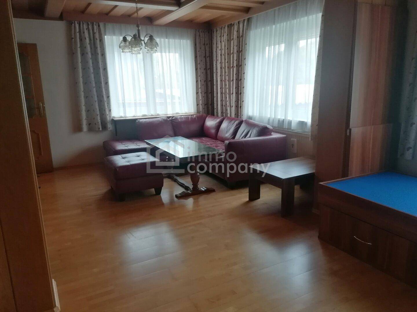 Wohnzimmer mit rotem Ecksofa, Holzboden und Holzdecke, bietet eine gemütliche Atmosphäre.