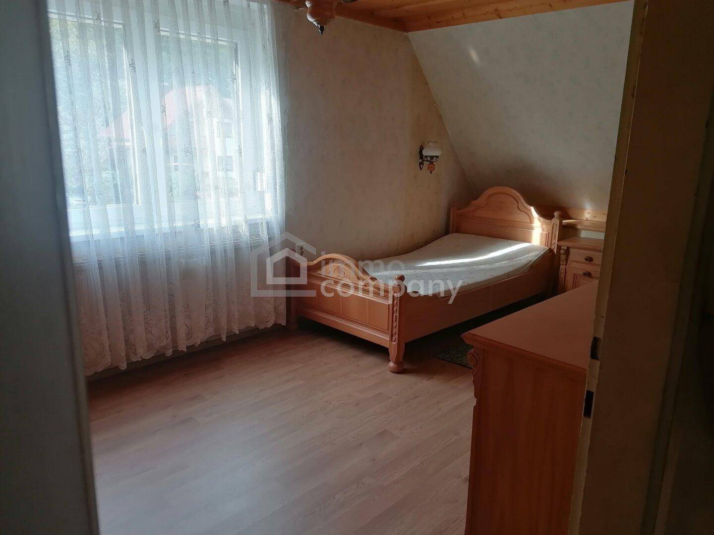 Schlafzimmer mit Einzelbett, Holzmöbeln und Dachschräge, hell durch großes Fenster.