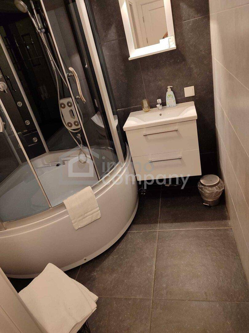 Modernes Badezimmer mit dunklen Fliesen, einer Duschkabine und einem einzelnen Waschbecken.