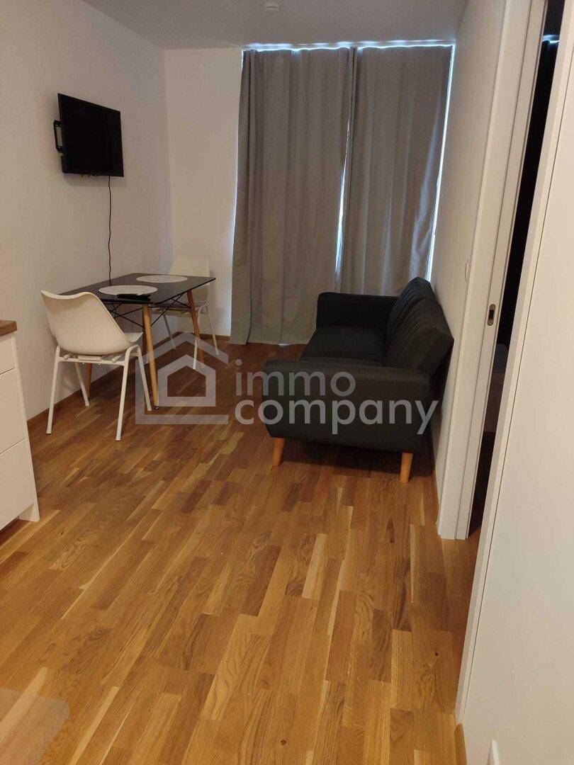 Gemütlicher Wohnbereich mit Sofa, kleinem Esstisch und viel Tageslicht durch große Fenster.