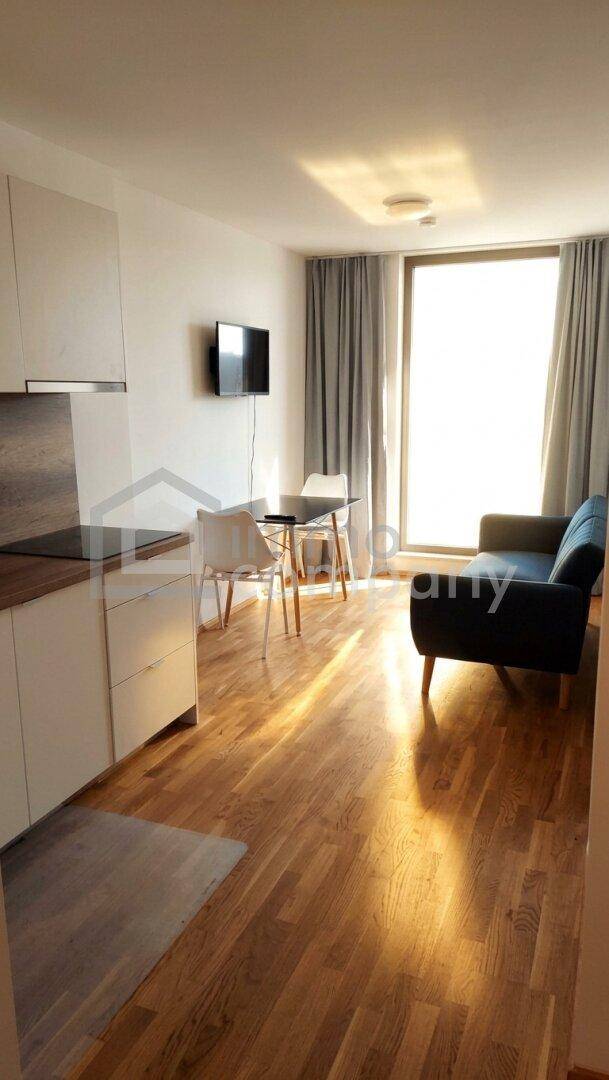 Heller Wohn- und Essbereich mit Holzboden, Sofa, Esstisch und großen Fenstern.