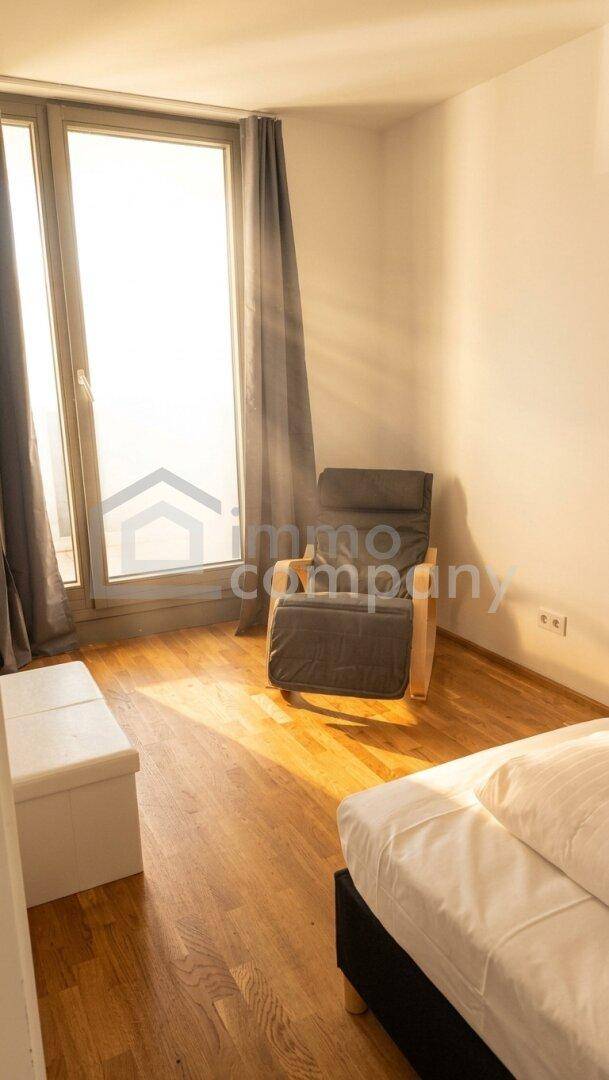 Helles Schlafzimmer mit Holzboden, einem Sessel und einem großen Fenster für viel Tageslicht.