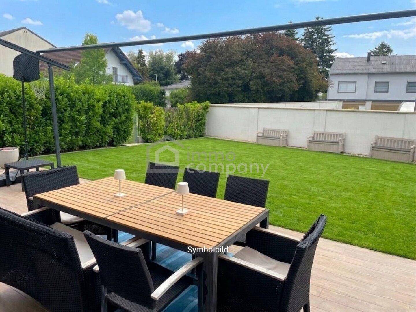 Gepflegter Garten mit Rasenfläche, Hecke und einem Essbereich auf der Terrasse.