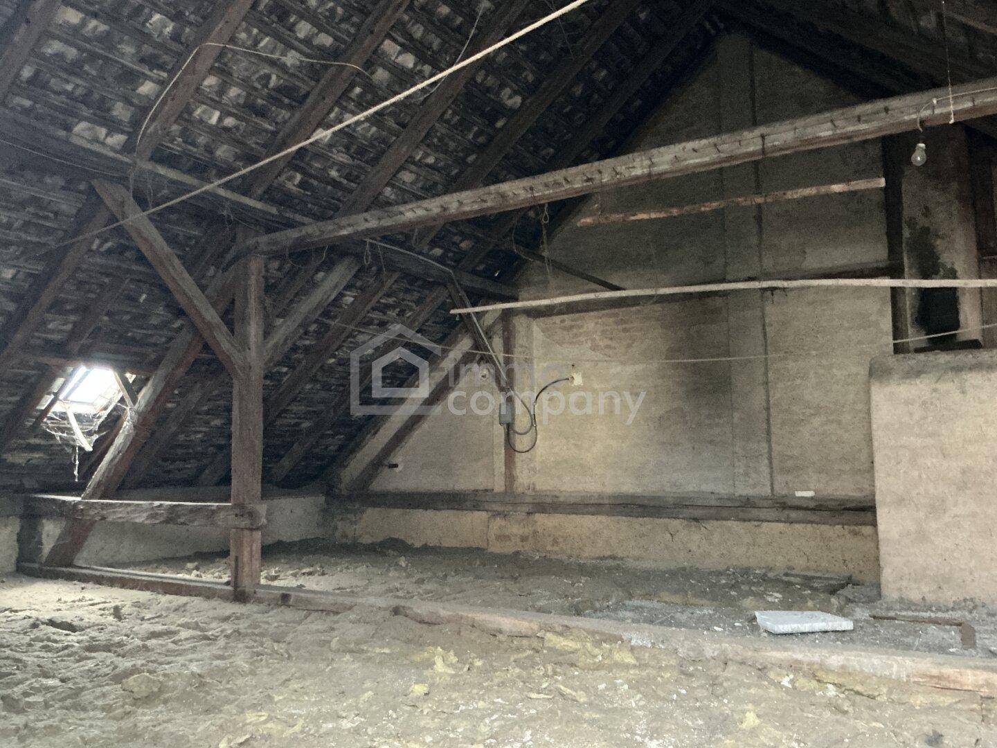 Unausgebauter Dachboden mit sichtbaren Holzbalken, Dachschräge und einem Dachfenster.