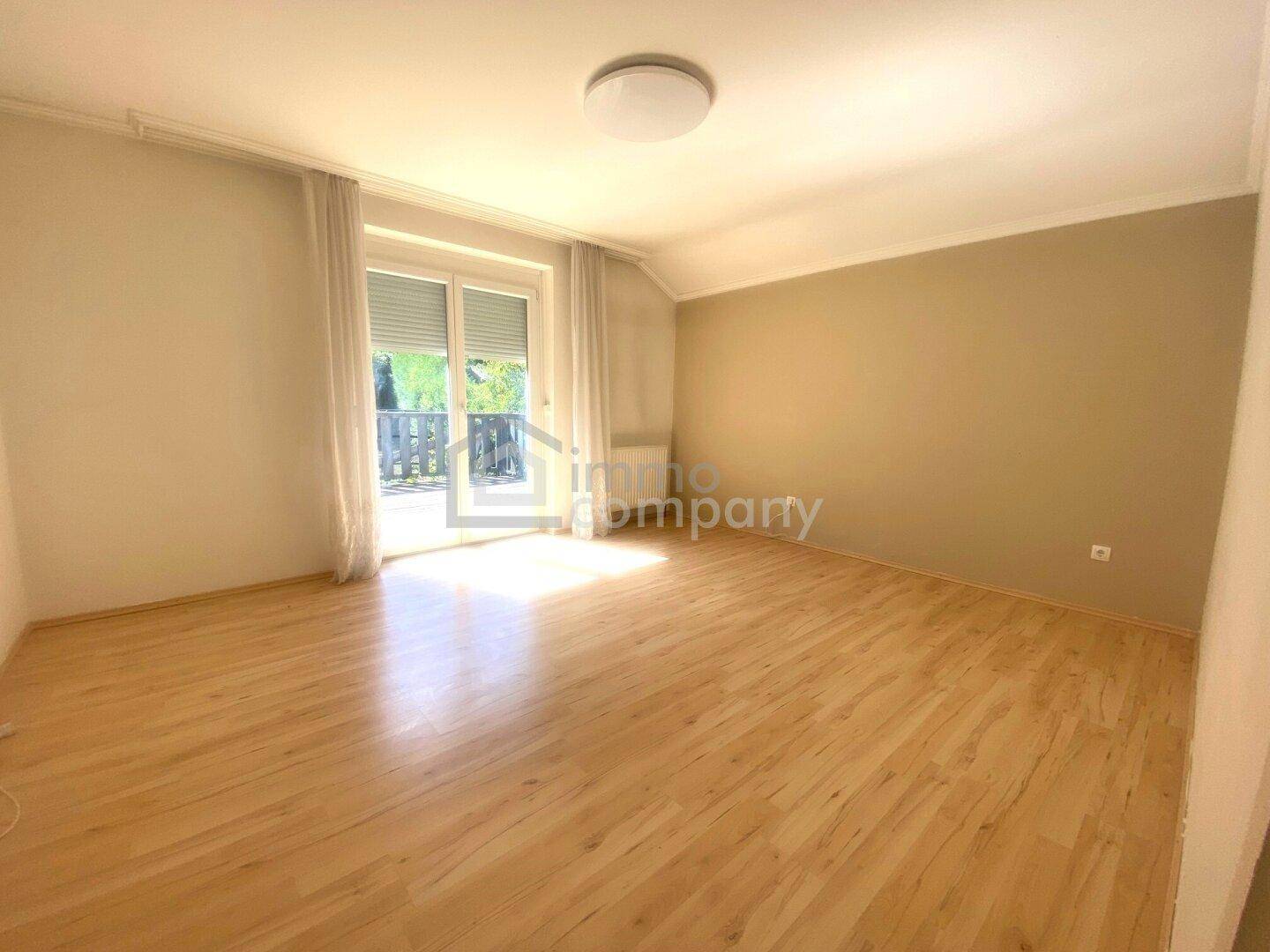 Geräumiges Schlafzimmer mit Holzboden und großer Schiebetür zum Balkon.