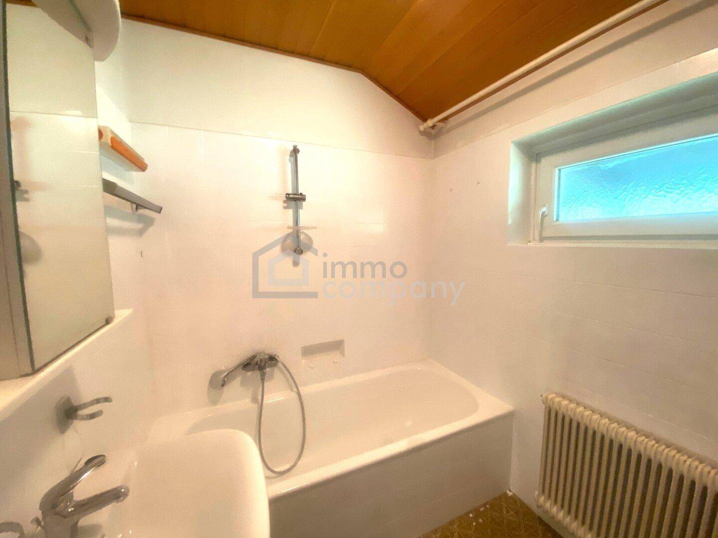 Helles Badezimmer mit Badewanne, Fenster und Holzverkleidung an der Decke.