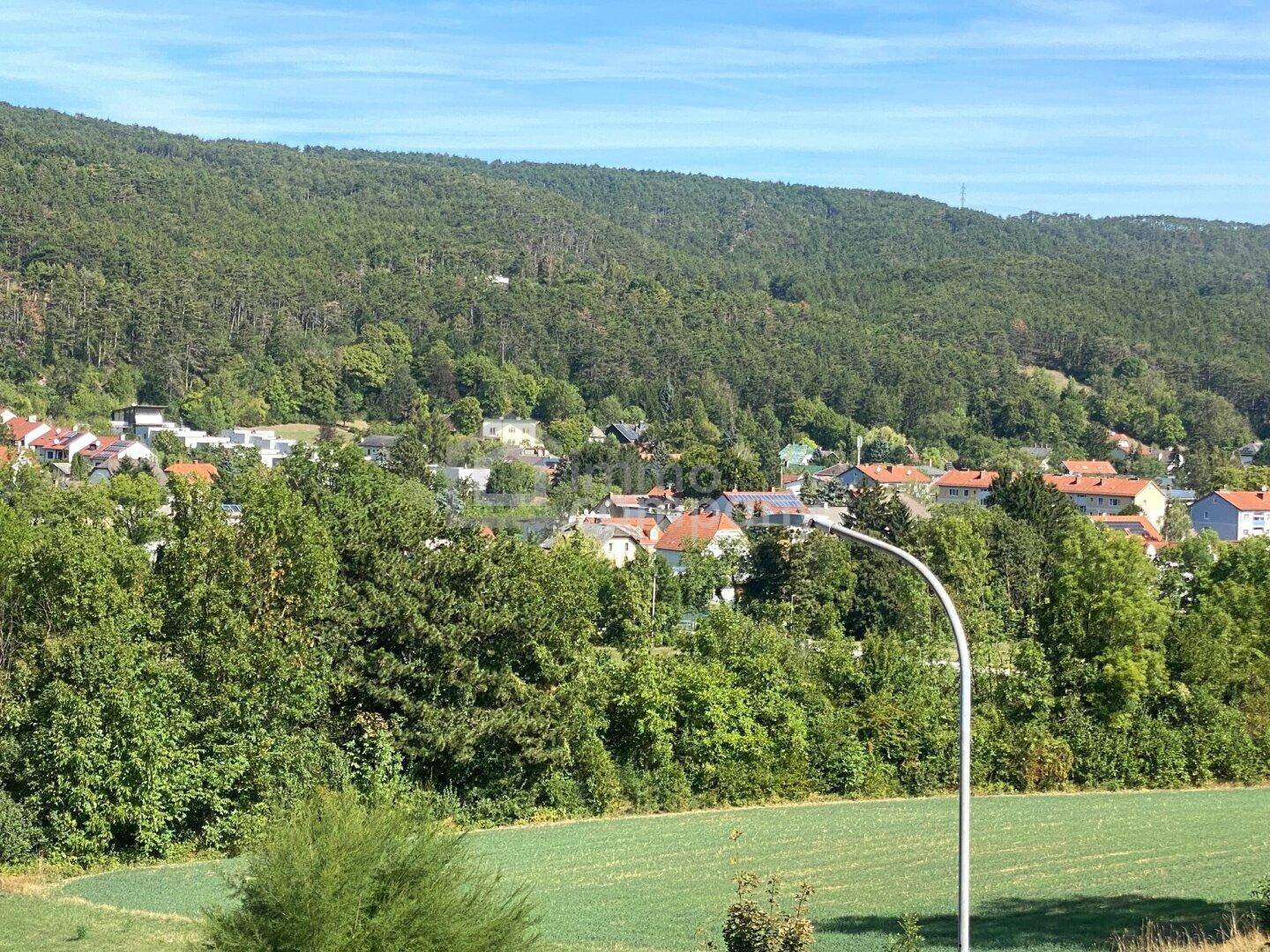 Panoramablick über eine ländliche Siedlung mit bewaldeten Hügeln im Hintergrund.