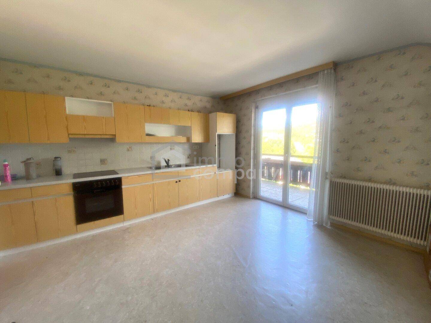 Helle Küche mit hellen Holzfronten, Einbauherd und Zugang zu einem Balkon.
