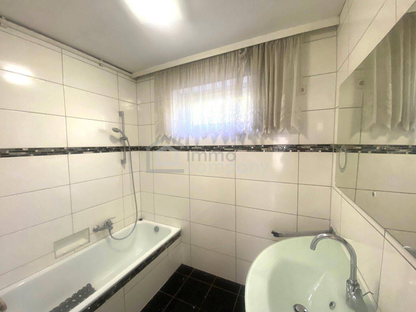 Gefliestes Badezimmer mit Badewanne, Waschbecken und einem Fenster.