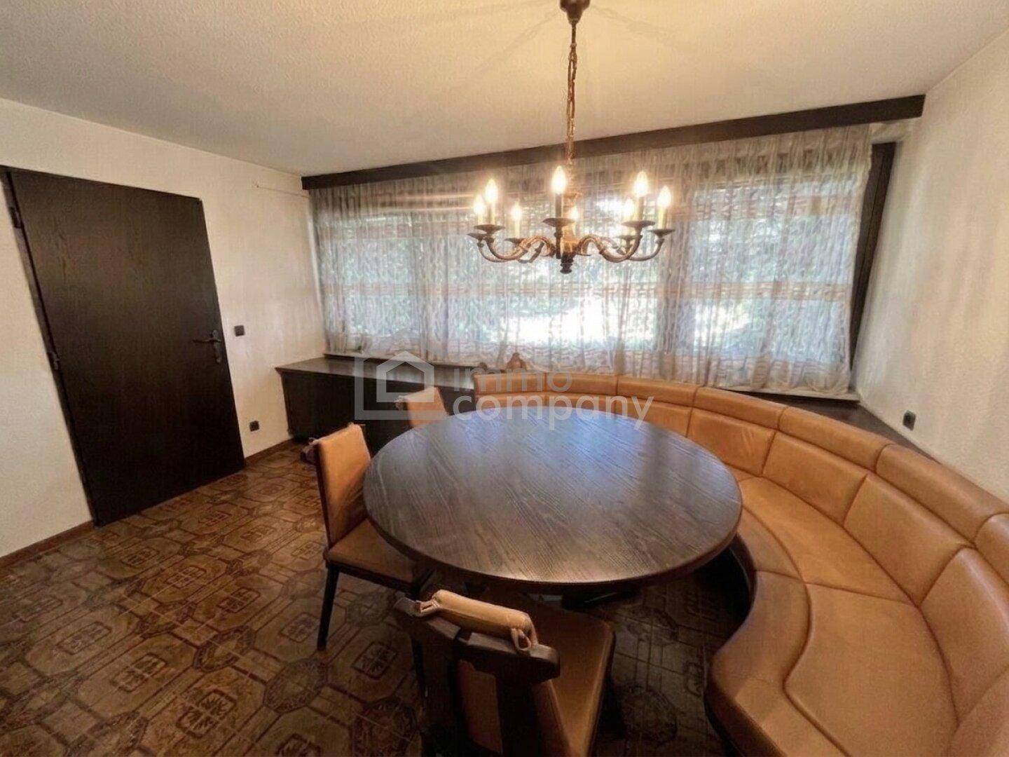 Essbereich mit runder Holztafel, eingebauter Sitzbank, gemusterten Fliesen und Kronleuchter.