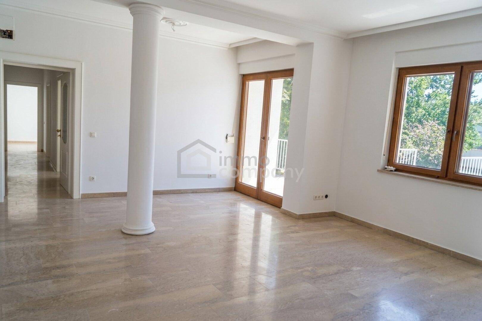 Geräumiger, leerer Wohnbereich mit Steinboden, einer Säule und Zugang zu einem Balkon.