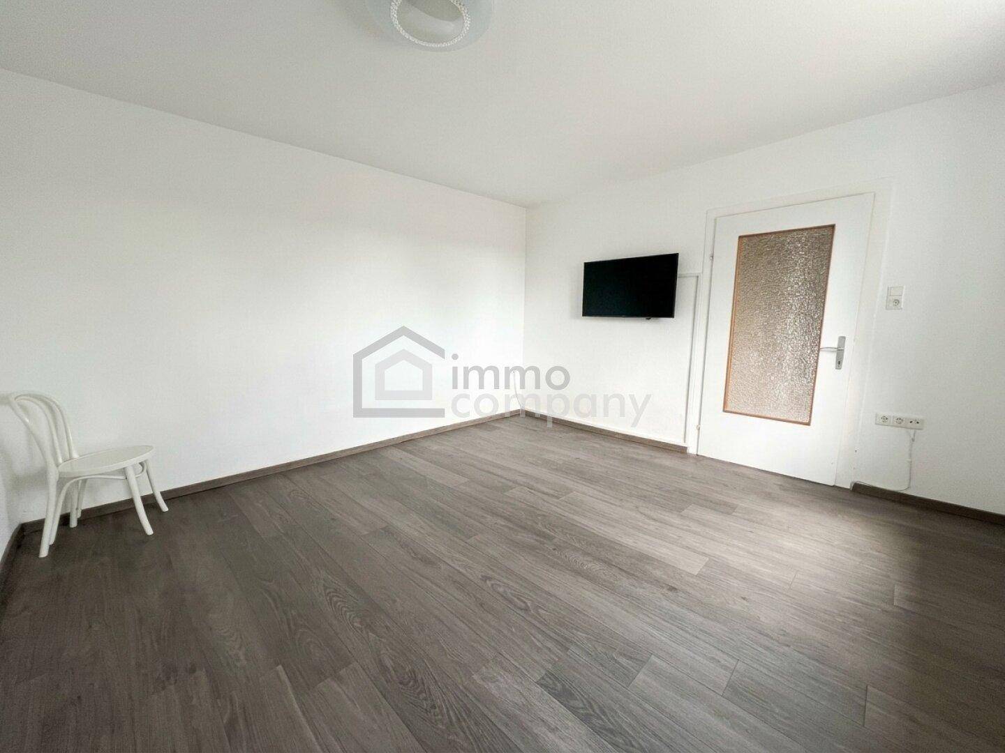 Leeres Zimmer mit modernem Laminatboden und weiß gestrichenen Wänden.