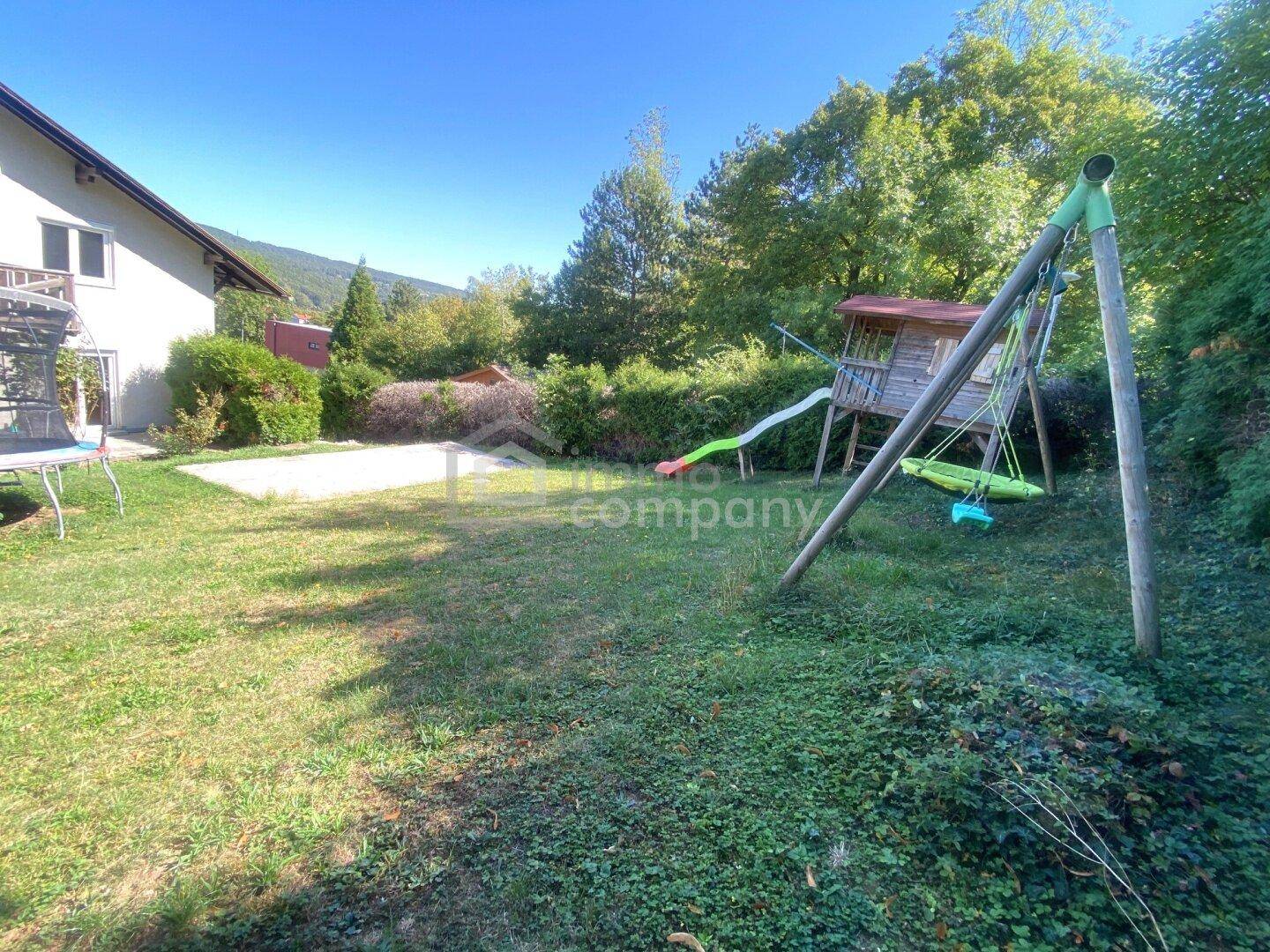 Großer Garten mit Rasenfläche und Kinderspielplatz, umgeben von Bäumen.