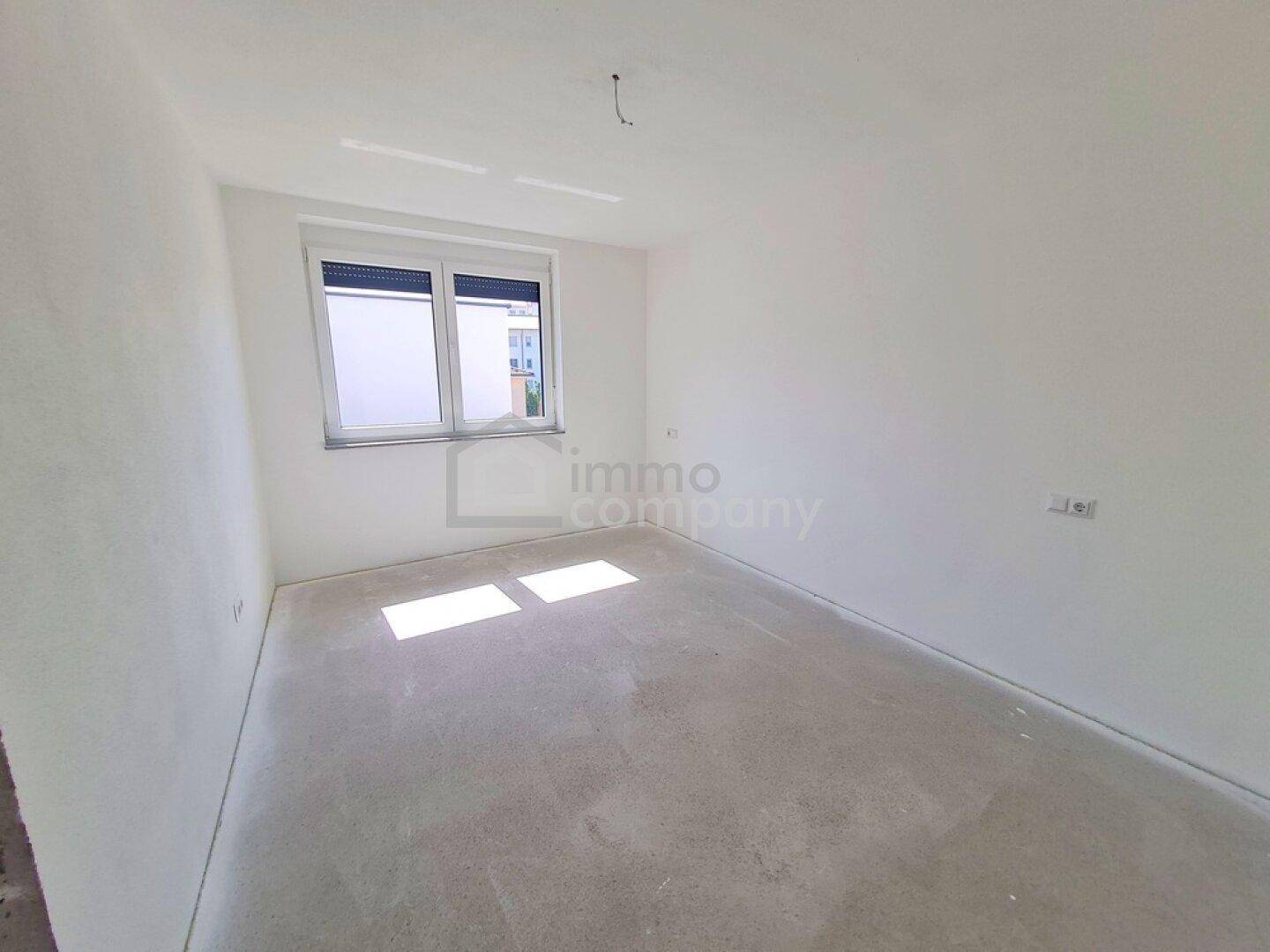Unmöbliertes Schlafzimmer im Neubau mit weiß gestrichenen Wänden und Betonboden.