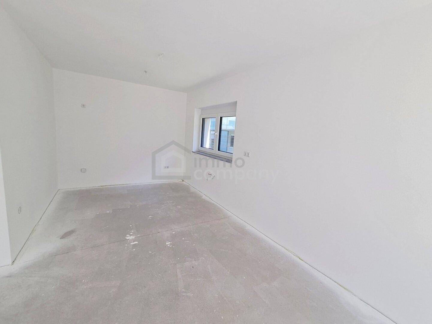 Weiteres unmöbliertes Zimmer im Neubau mit weiß gestrichenen Wänden und Betonboden.