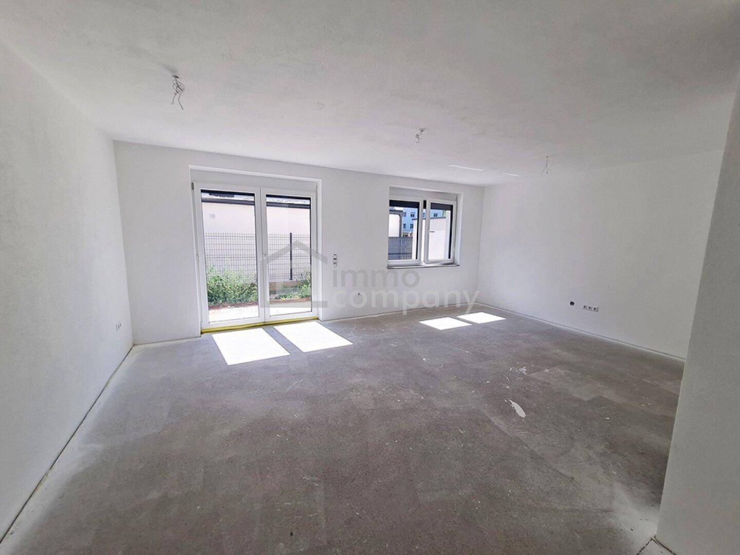 Heller, unmöblierter Wohnraum im Neubau mit Zugang zum Garten und großen Fenstern.
