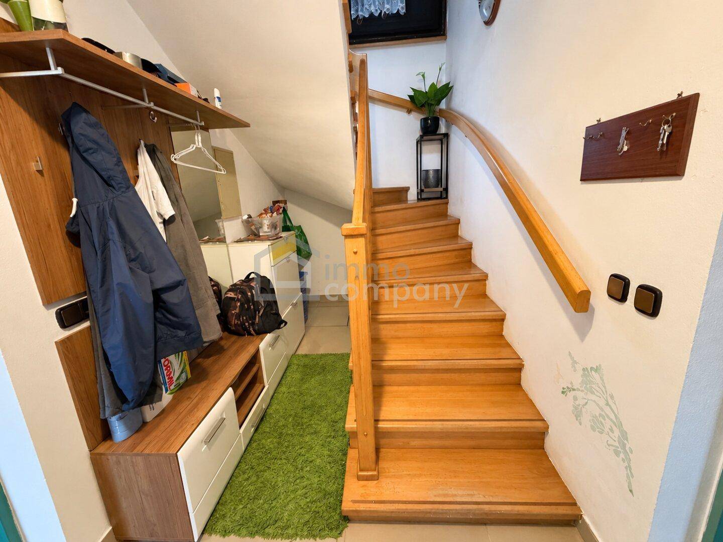 Heller Eingangsbereich mit Holztreppe, Garderobe und Stauraum unter der Treppe.
