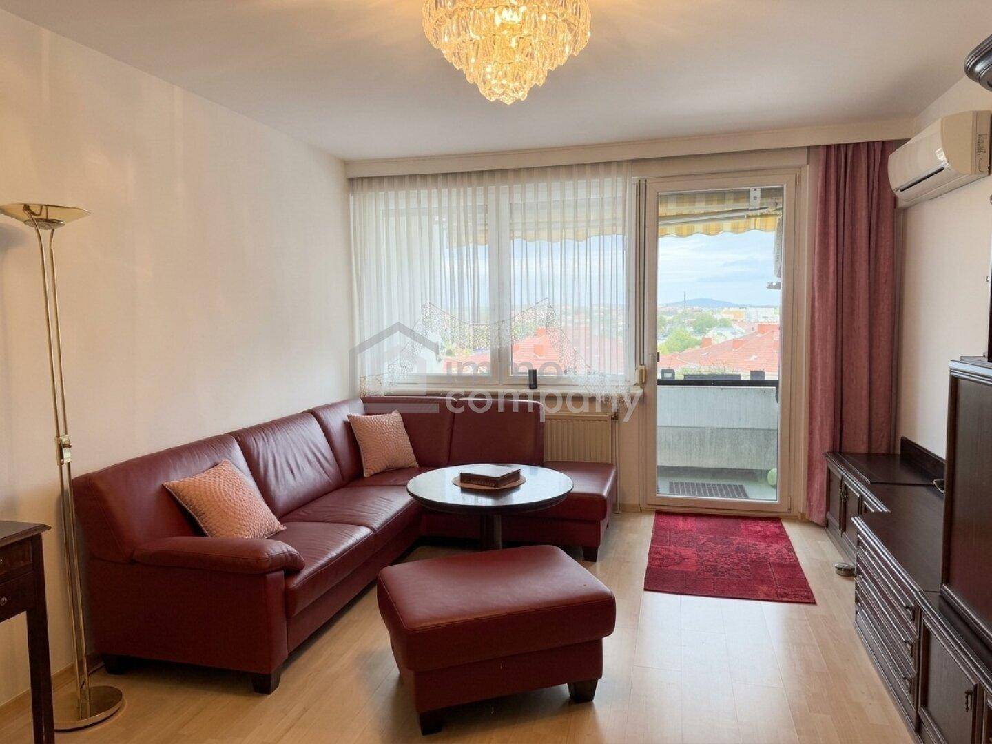 Helles Wohnzimmer mit rotem Sofa, Klimaanlage und Balkontür, die viel Tageslicht hereinlässt.