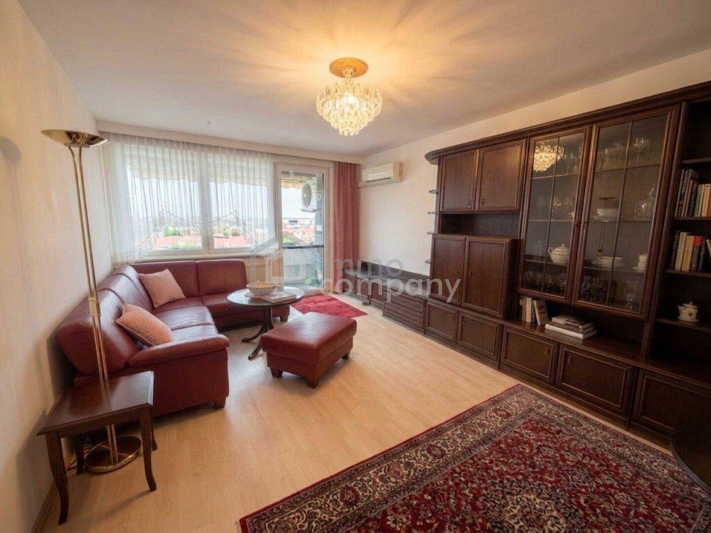 Gemütliches Wohnzimmer mit rotem Ledersofa, großem Holzschrank und Zugang zum Balkon mit Weitblick.