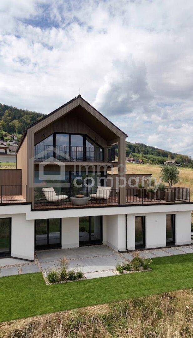 Modernes Haus mit großer Terrasse, Rasenfläche und Blick auf die umliegende Landschaft.