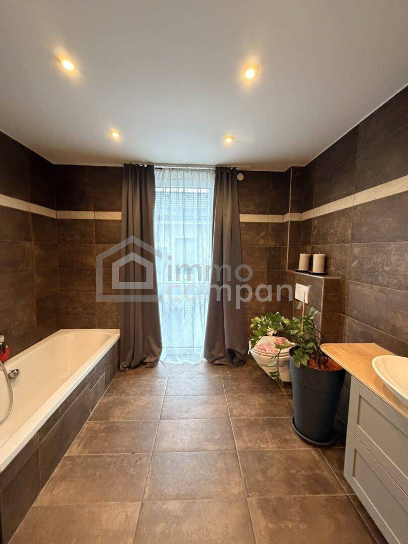 Geräumiges Badezimmer mit dunklen Fliesen, Badewanne und einem Fenster für natürliches Licht.