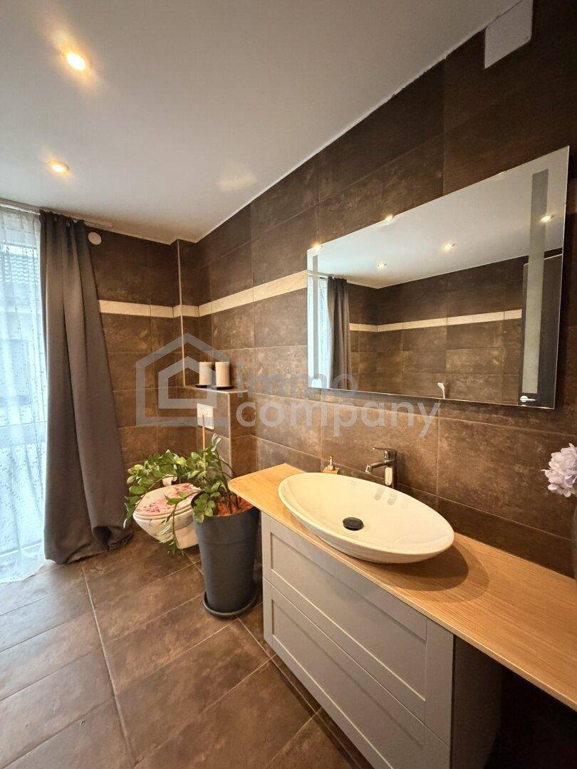Badezimmer mit dunklen Fliesen, modernem Aufsatzwaschbecken und großem beleuchteten Spiegel.