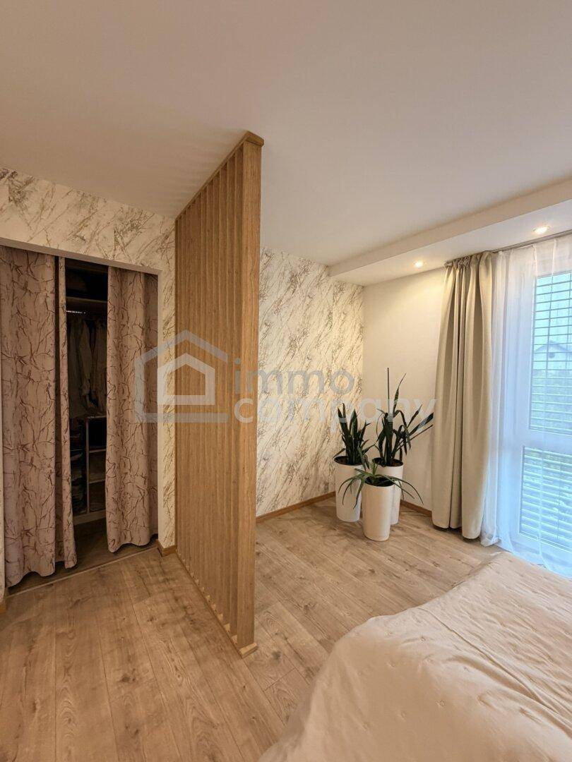 Schlafzimmer mit Holzboden, dekorativer Trennwand und Zugang zu einem begehbaren Kleiderschrank.
