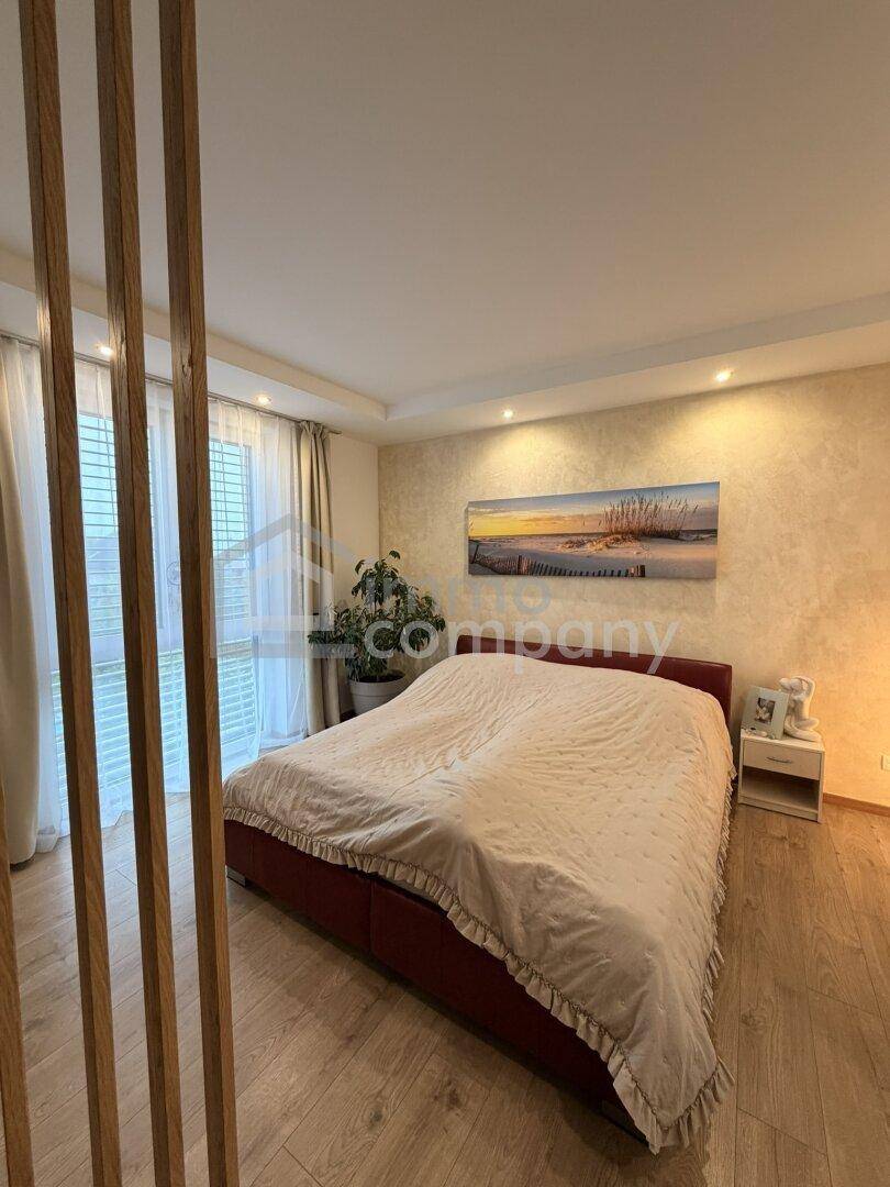Geräumiges Schlafzimmer mit Holzboden, großem Bett und Blick auf den Garten durch die Fenster.